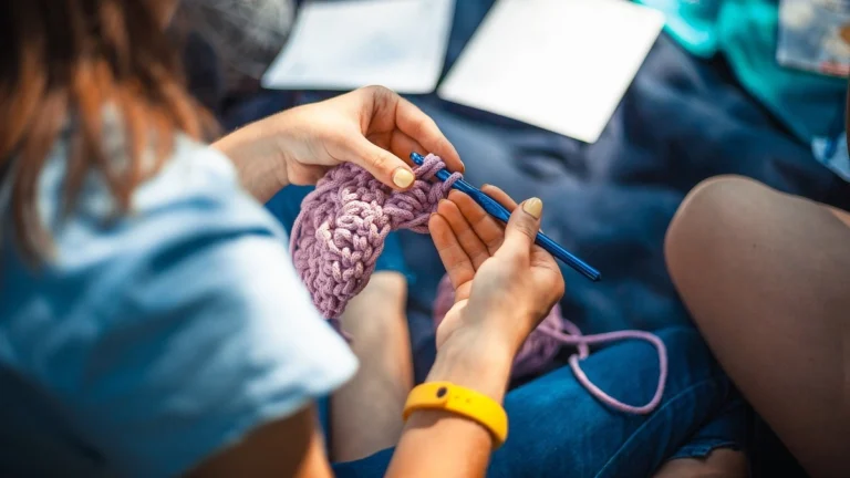 A person working on a crochet project, in the background a crochet pattern is visible.